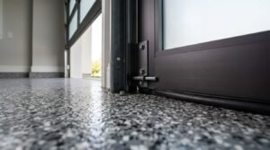 Close-up of a glossy decorative epoxy flake garage floor meeting a heavy-duty modern garage door frame and structural mounting hardware.