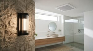 Modern bathroom lighting featuring a contemporary black sconce mounted on a textured stone accent wall, accompanied by a ceiling ventilation fan to control humidity and prevent moisture damage.