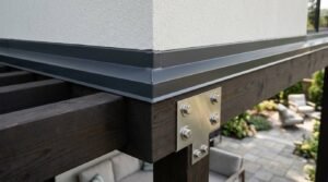 Close-up of dark grey metal flashing installed along stucco wall base above a dark wood timber frame with steel T-bracket connector