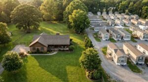 Aerial view comparing a large single-family traditional house on a green lawn next to a park model and manufactured home community