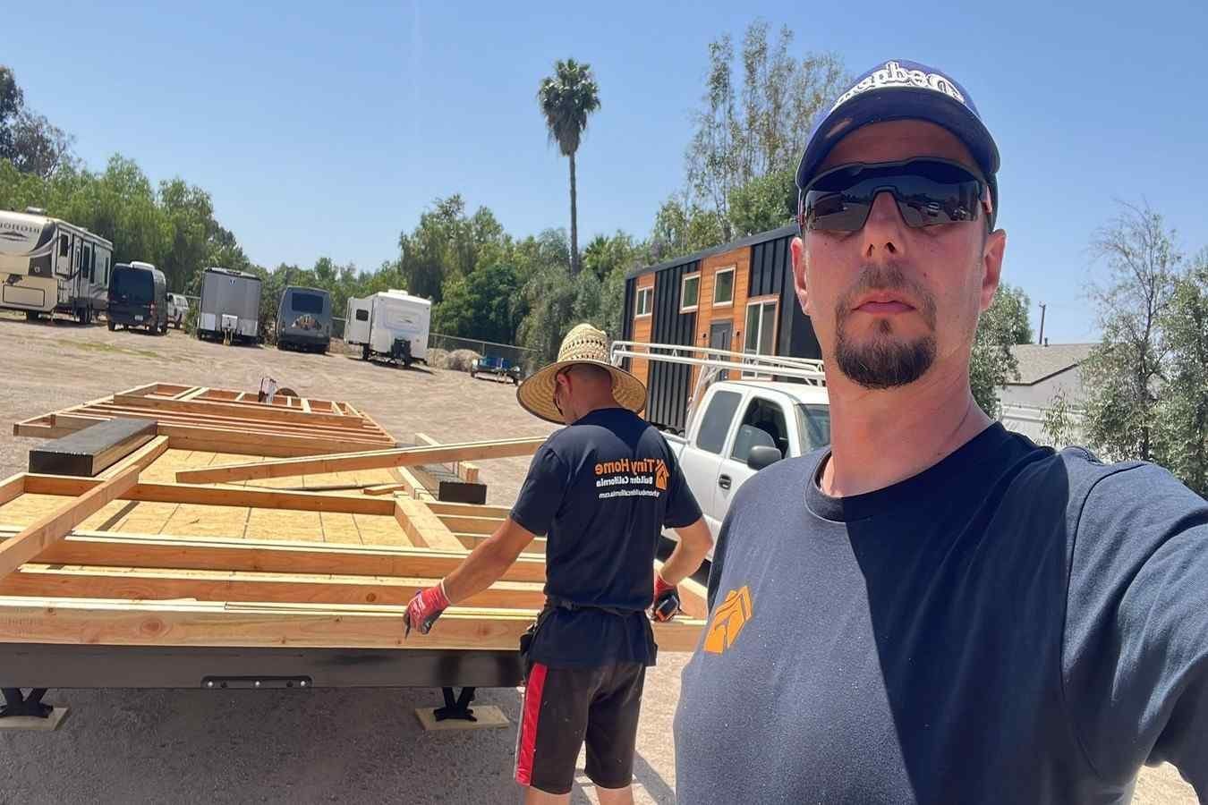 Tiny home construction crew assembling a trailer frame at an outdoor fabrication yard.