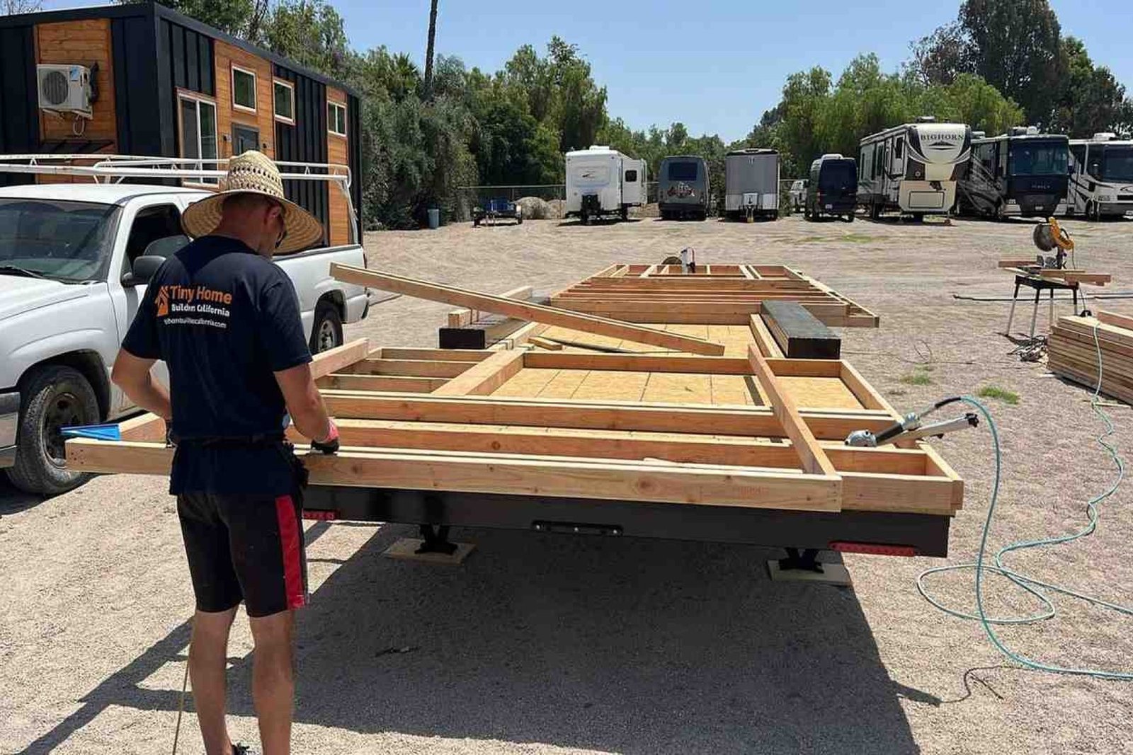 Tiny home builder framing a trailer foundation at an outdoor construction yard.