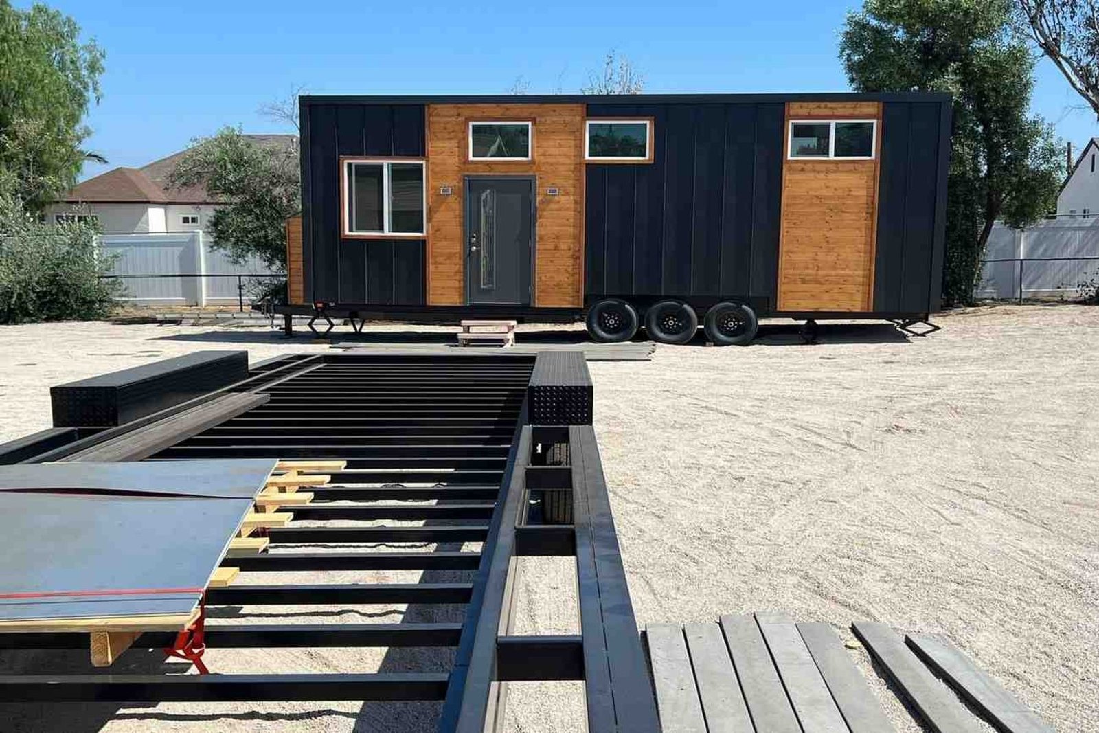 Tiny house on wheels with black metal siding, wood accents, and custom steel trailer frame.