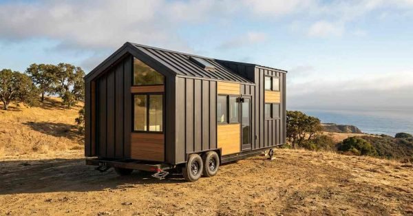 Modern tiny home on wheels showcasing durable exterior siding, wood accents, metal roofing, large windows, and a dual-axle trailer frame.